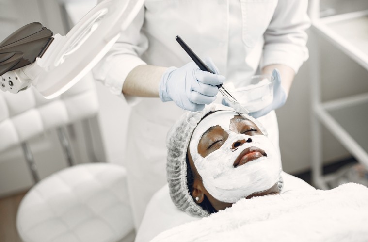 A gloved practitioner applying a facial mask to a client resting with her eyes closed